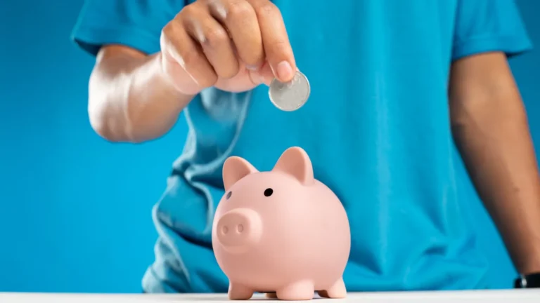 A hand dropping a coin into a piggy bank